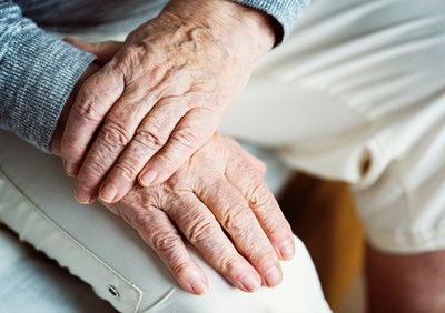 Et par hænder på en ældre person. Personen holder sit ene håndled med den anden hånd.