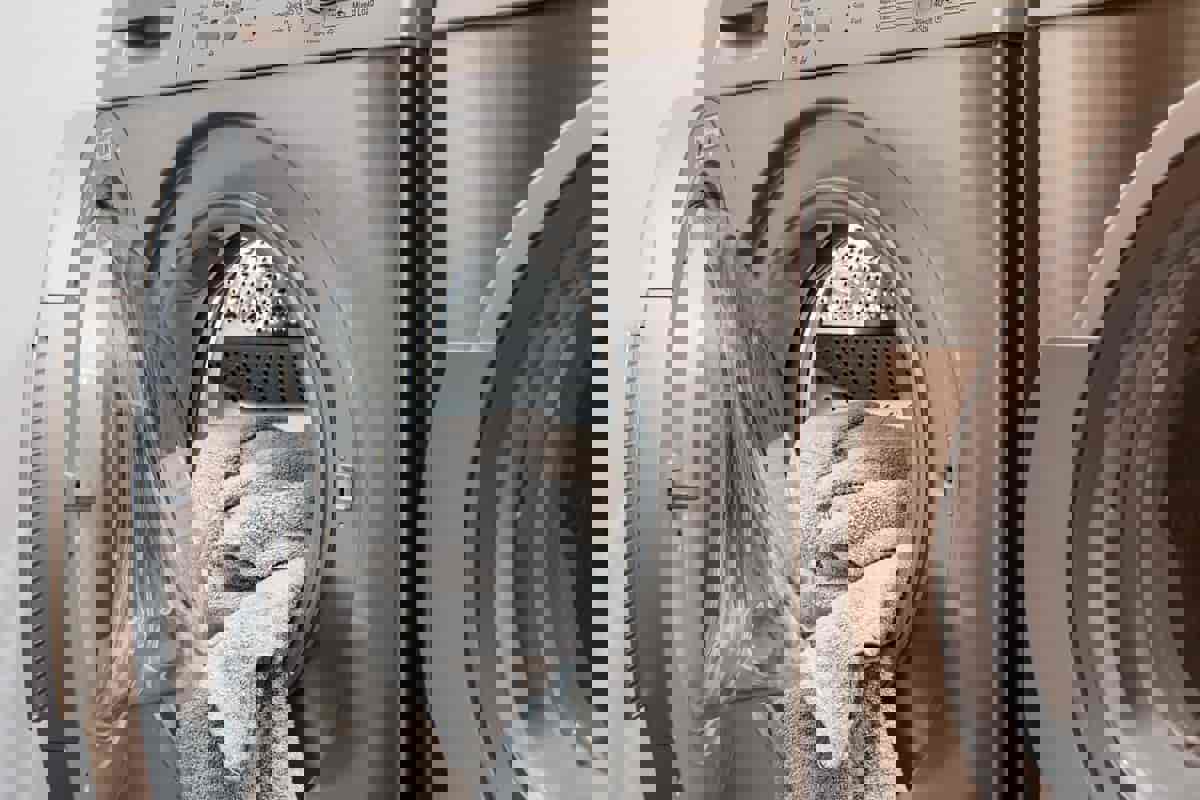 En sølvfarvet vaskemaskine. Der ligger et håndklæde i maskinen, som lågen ikke er lukket på endnu.