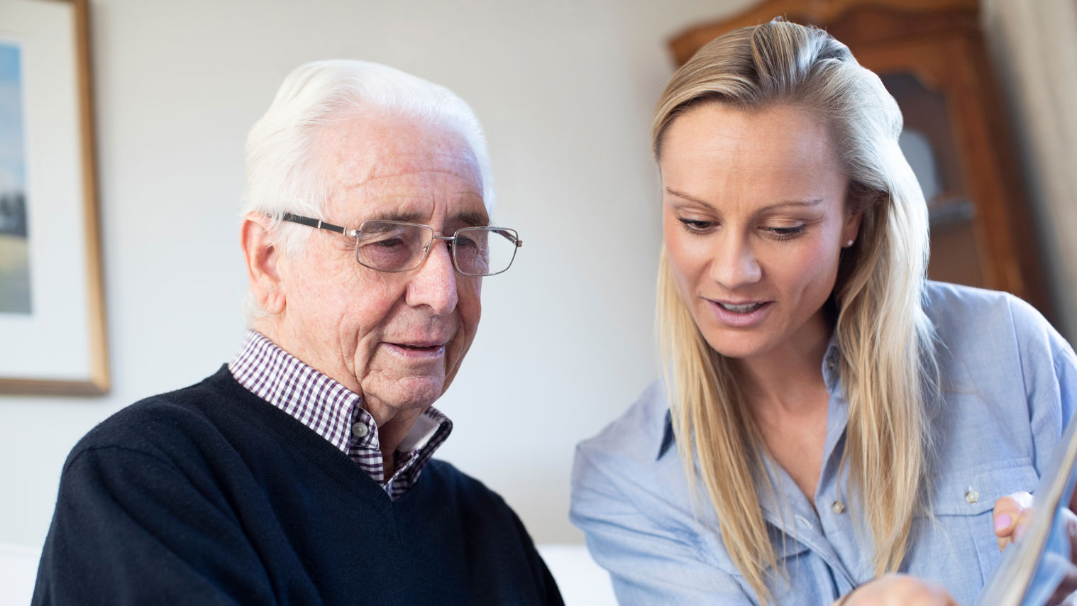 Ældre mand kigger på billeder med en lyshåret kvinde. Kvinden peger på et billede. Manden ser ud til at genkende det.